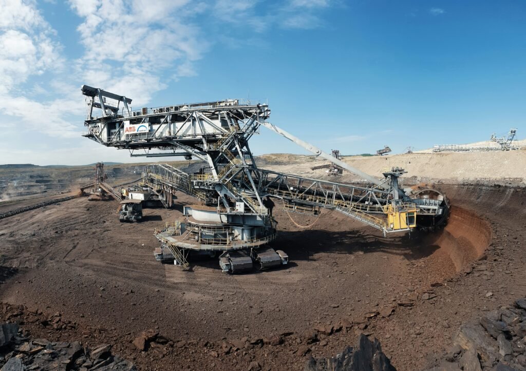 Modern gold mining equipment including excavators, haul trucks, crushers, and drilling machines operating at an industrial mining site.